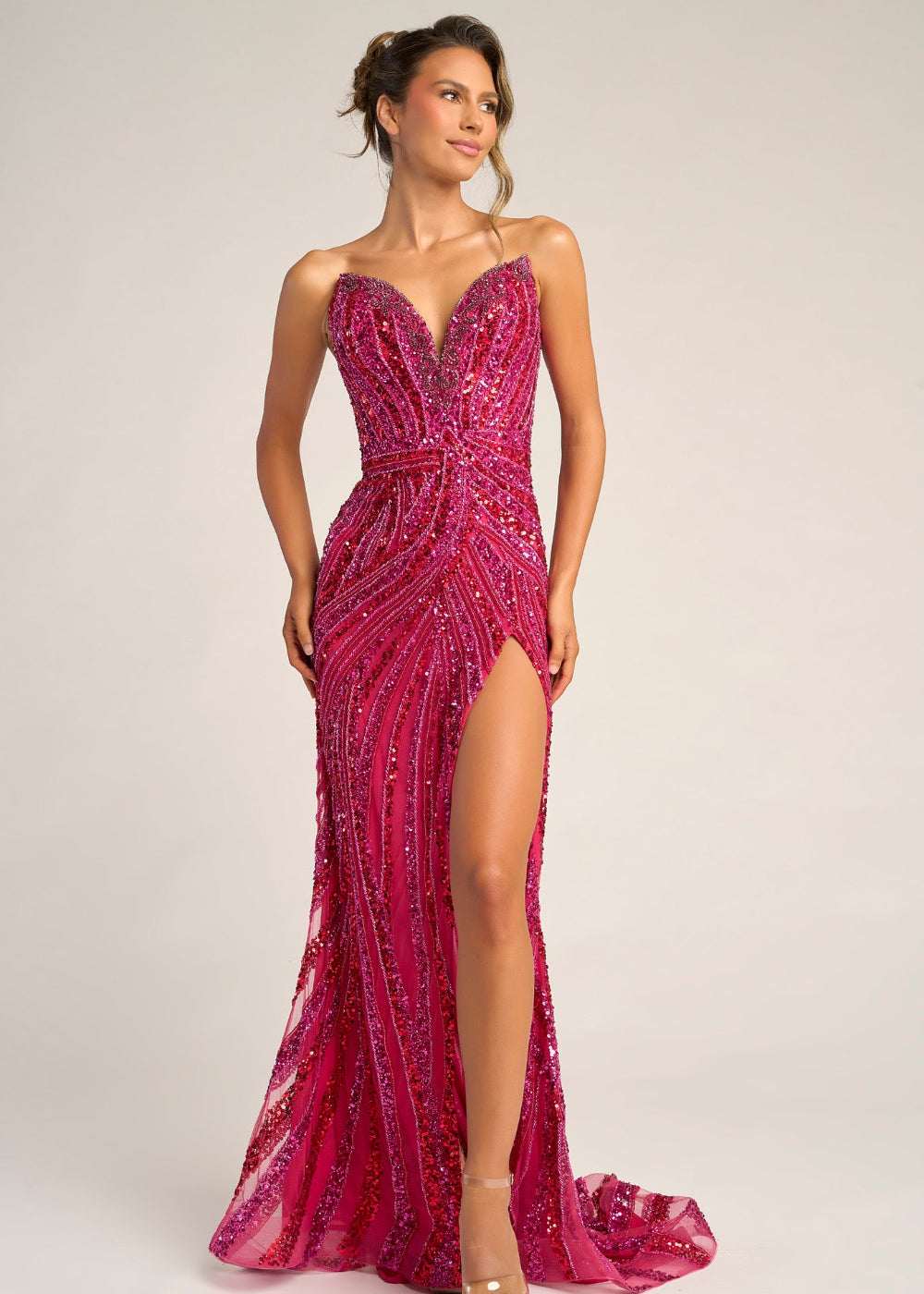 Woman wearing a pink beaded evening gown with a slit on a plain background