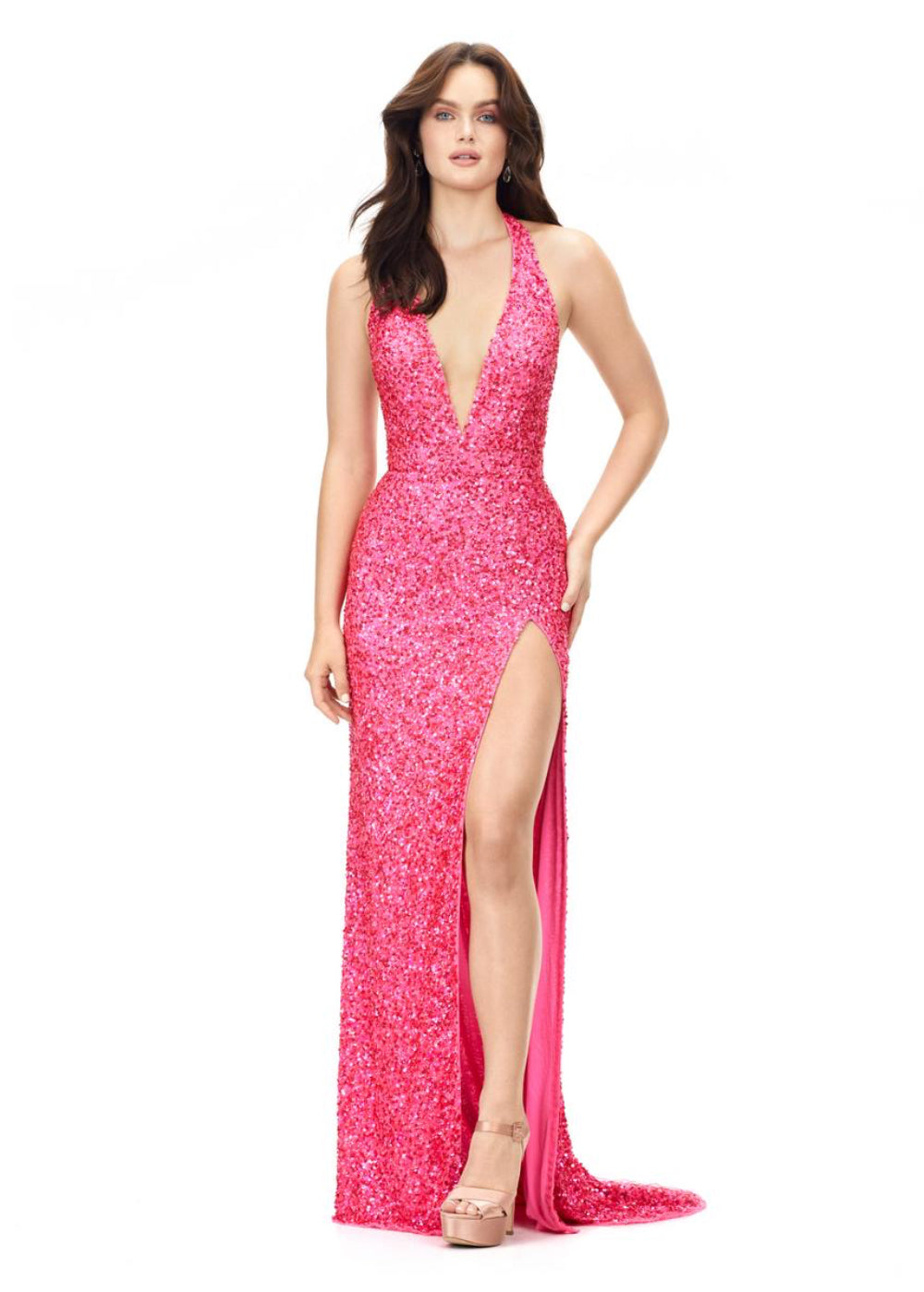 A woman wearing a pink, sequined, V-neck gown with a high slit on the left side. The gown is form-fitting and floor-length, and she is posing with one hand on her hip.