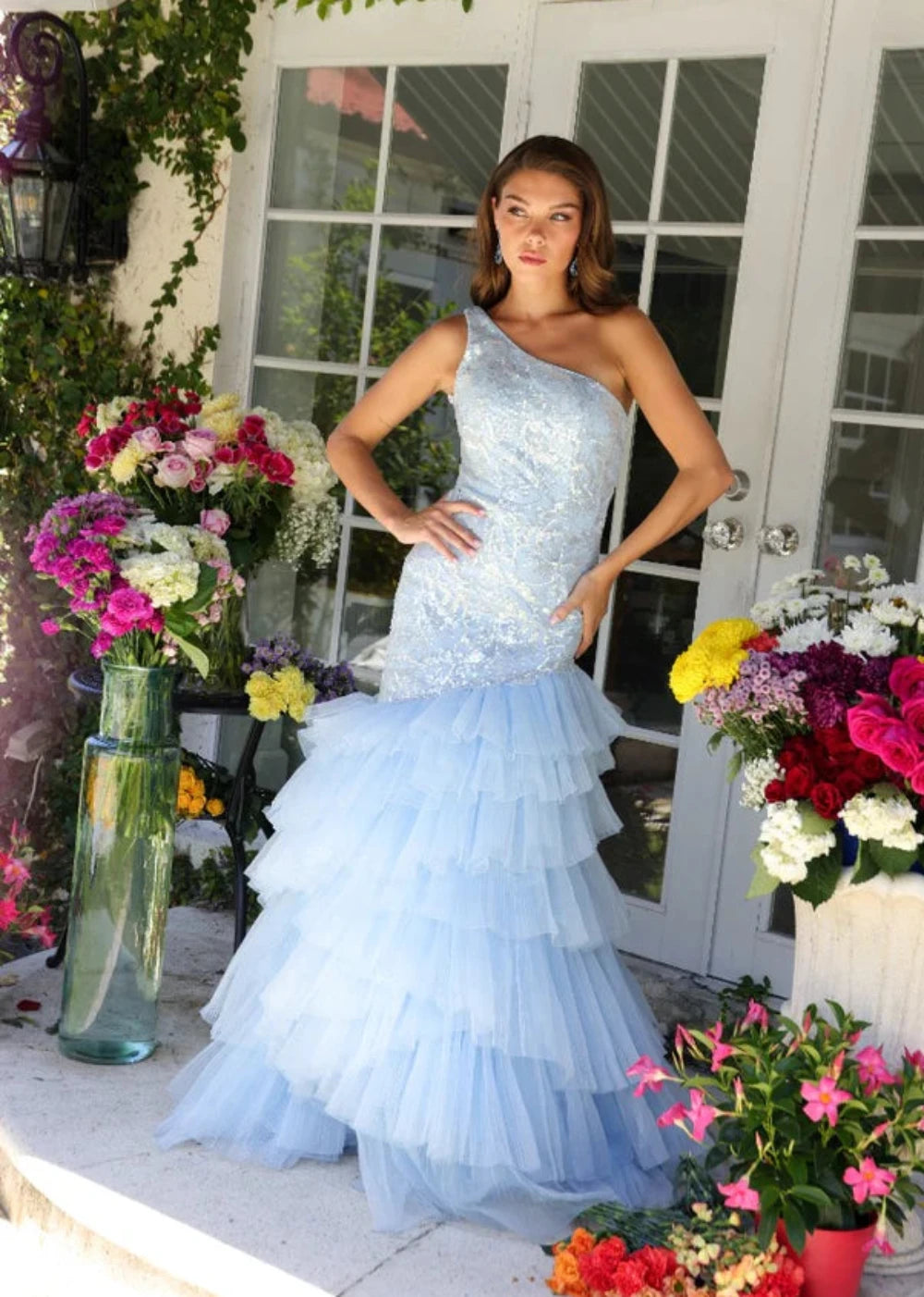 A woman in a blue formal dress posing in front of a floral arrangement.