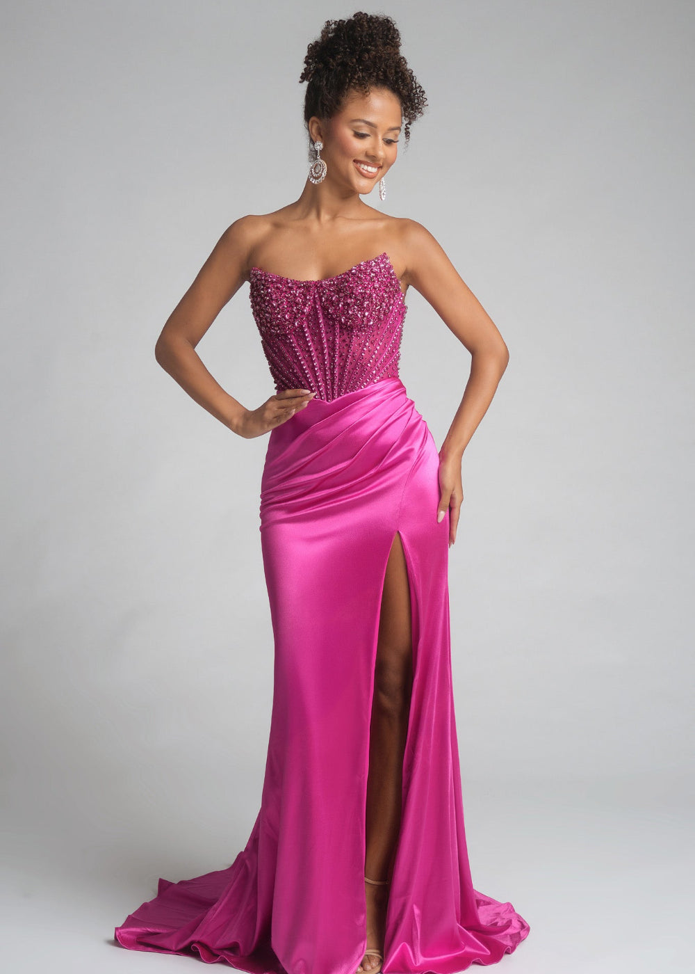 Woman wearing a pink strapless gown with a slit on a gray background