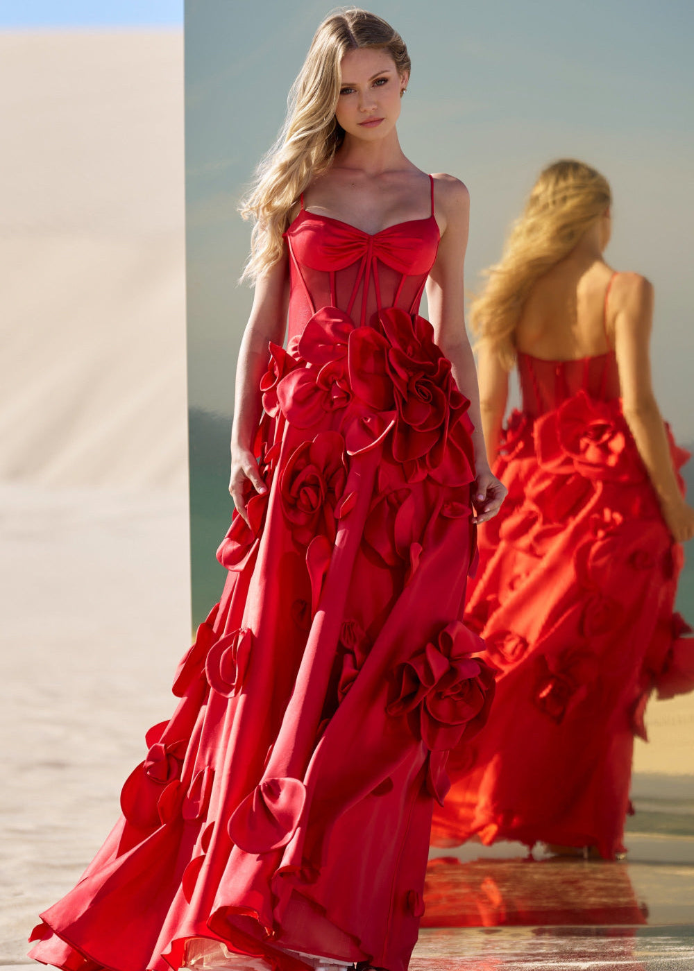 Woman wearing a red floral dress walking on a sandy surface.
