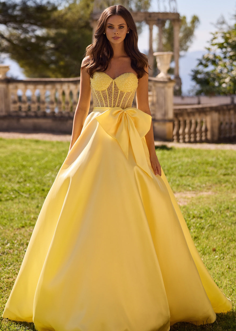 A woman wearing a yellow Sherri Hill 57035 evening gown with a sweetheart neckline and a bow detail at the waist.