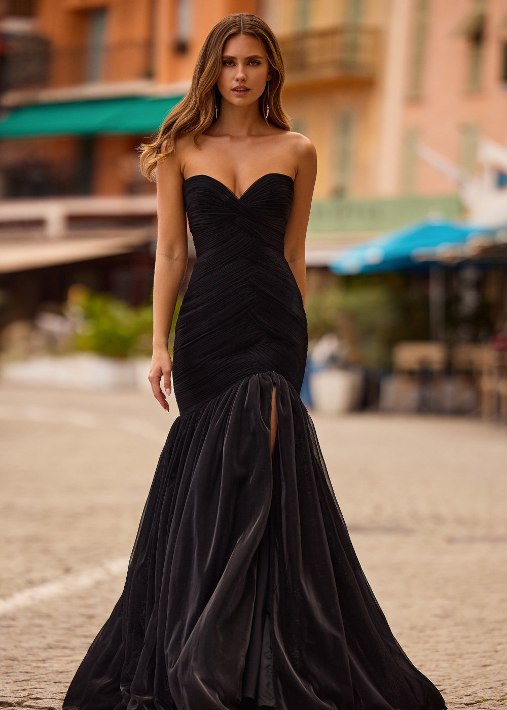 A woman wearing a black, strapless, mermaid-style evening dress with a sweetheart neckline and a split at the front.