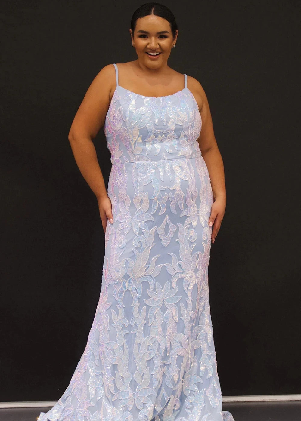 Woman wearing a light blue lace evening gown against a black background